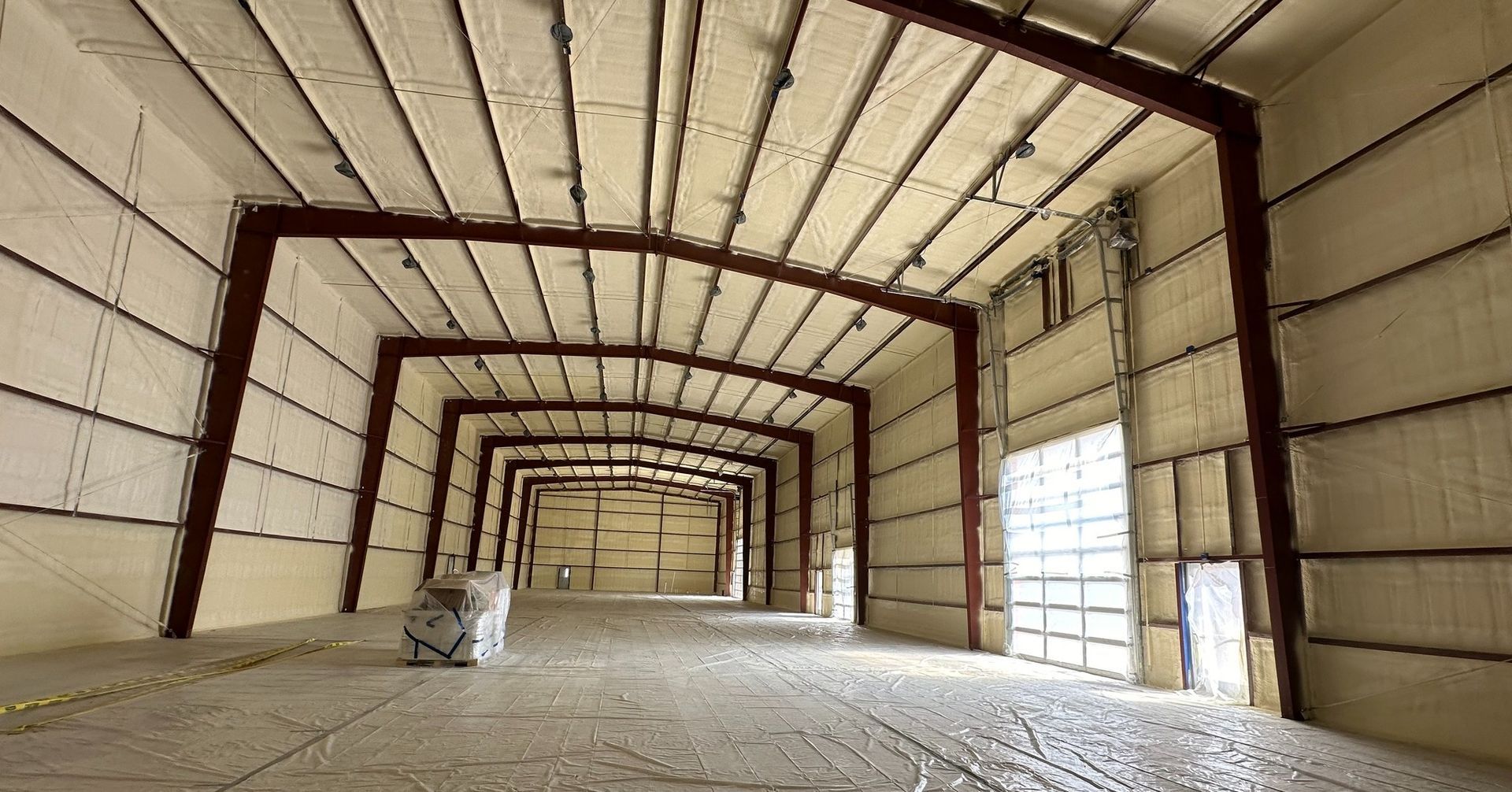 Empty industrial warehouse with metal beams, insulated walls, and a concrete floor