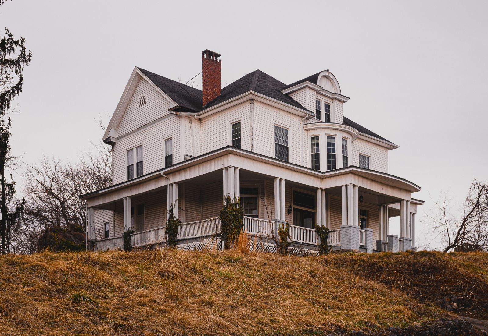 Classic older white two-story home with wraparound porch in late autumn